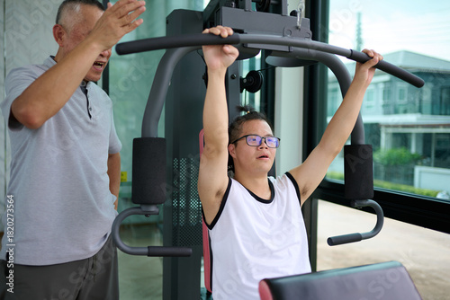 A trainer assisting a young man with down syndrome as he exercises on a weight machine at the gym