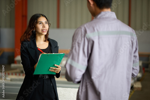 Businesswoman and engineer in a factory, with one person taking notes on a clipboard
