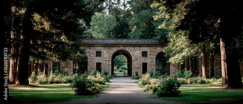 Stone garden building with arched entryway centered on a gravel path surrounded by tall trees and lush greenery