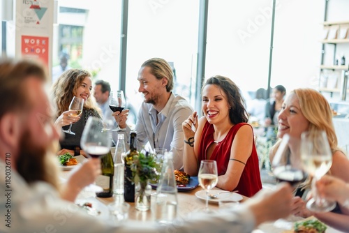 Фотография A diverse group of friends enjoying a lively dinner party share laughter, wine, and delicious food in a warm atmosphere