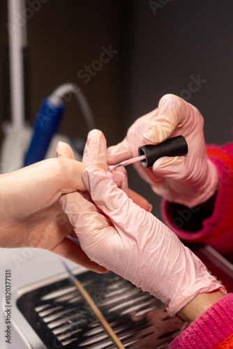 Manicure polish. Professional nail treatment. Master female manicurist hands in pink latex protective gloves applying acrylic gel.