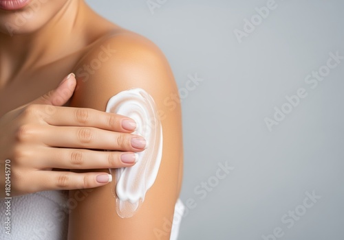 Female hand applying luxurious white body lotion to a smooth shoulder for skin care.