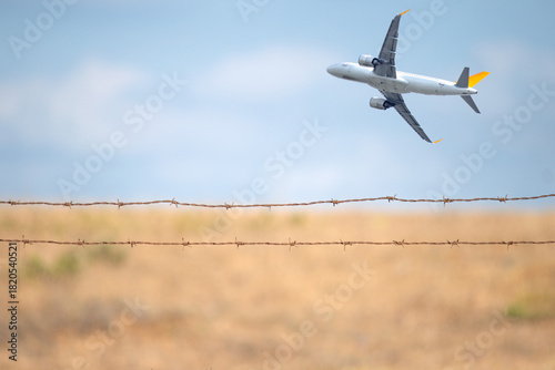 Passenger plane taking off behind wire fence. Concept of cross border or international travel. Aviation. Airport runway safety barrier. Deported. Copy space, blank, empty. 