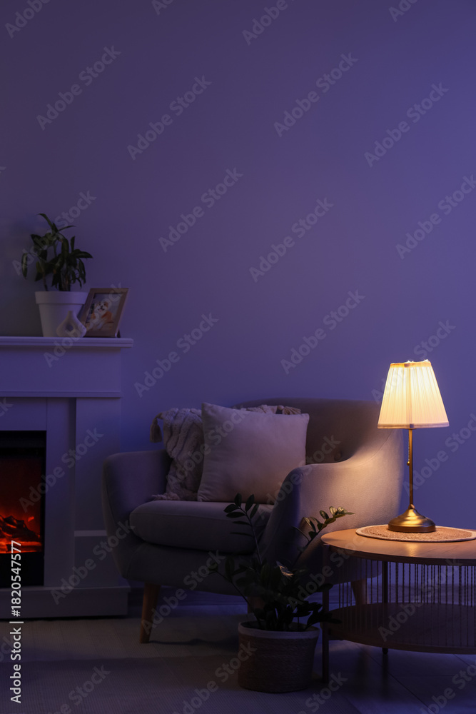 Fototapeta premium Interior of dark living room with glowing lamp, armchair and fireplace at night