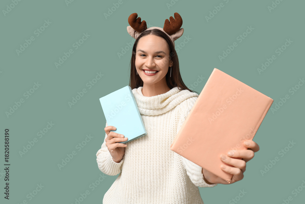 Naklejka premium Happy young woman in Christmas reindeer horns with books on turquoise background