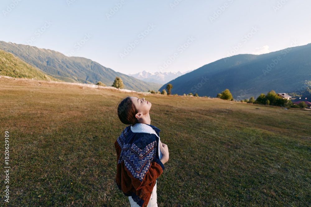 Naklejka premium Girl with backpack standing in sunlit meadow looking up at distant mountains and valley, enjoying nature and rural landscape, freedom, exploration and a peaceful outdoor moment.