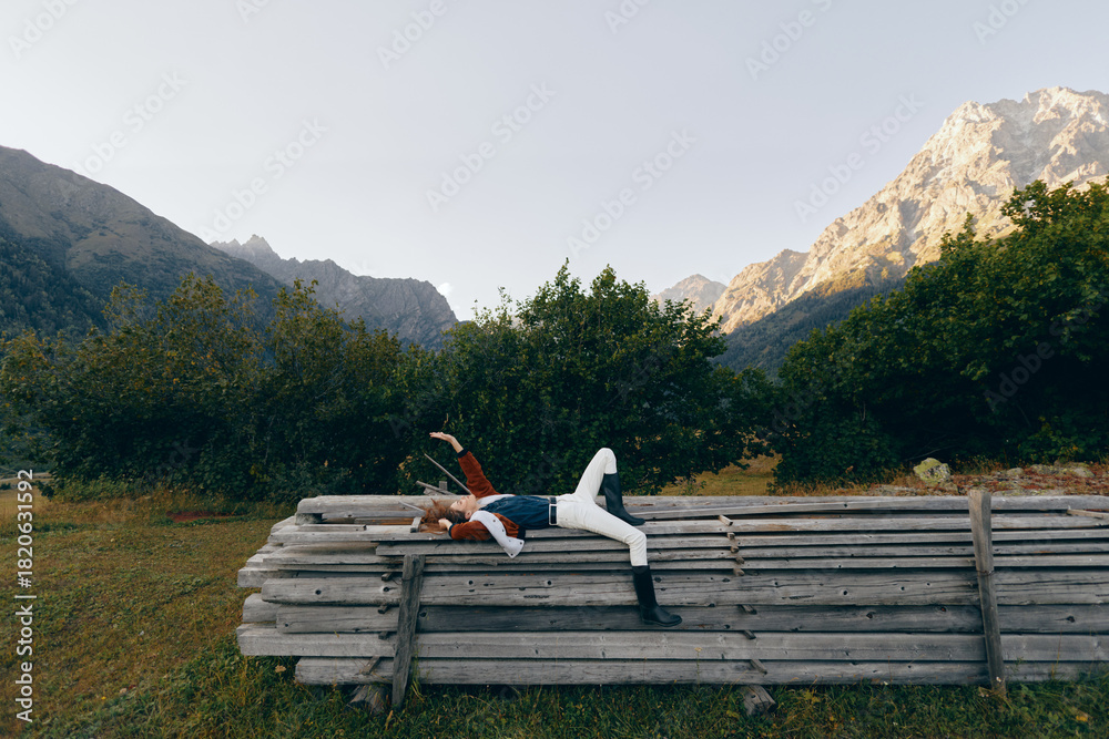 Fototapeta premium Person woman lying on stacked logs in a meadow, enjoying nature and mountains view, relax outdoors among trees and wooden pile for peaceful countryside rest and leisure.
