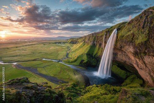Panoramic vista of a waterfall cascading down a cliff face at sunset over a valley