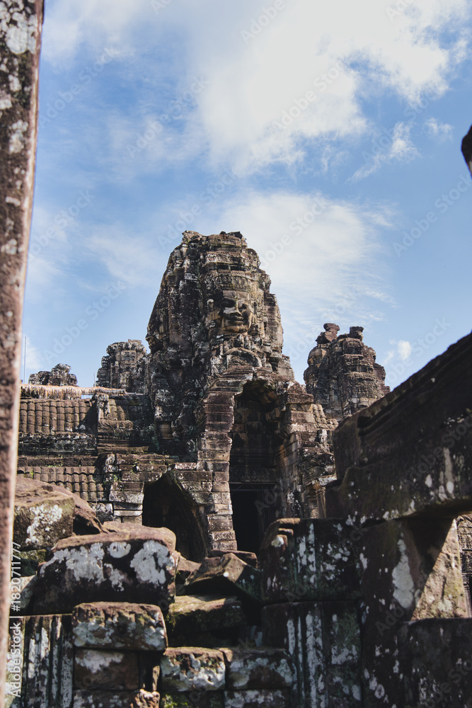 Fototapeta premium Ancient stone faces with serene expressions intricately carved on the tower of bayon temple, overlooking the rich archaeological complex of angkor thom in siem reap, cambodia