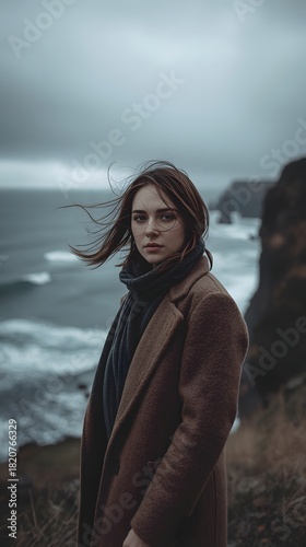 Moody portrait of woman standing on windy cliff above dramatic ocean waves