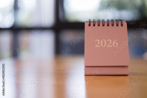 Close-up of pink desk calendar showing year 2026 on wooden table. Minimal design concept for planning, new year goals, future events, time management personal organization themes.