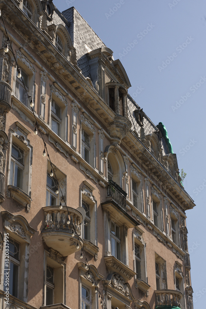 Fototapeta premium Detail of a richly decorated historic tenement house facade, showcasing ornate balconies, sculptural elements, and a classic mansard roof against a blue sky