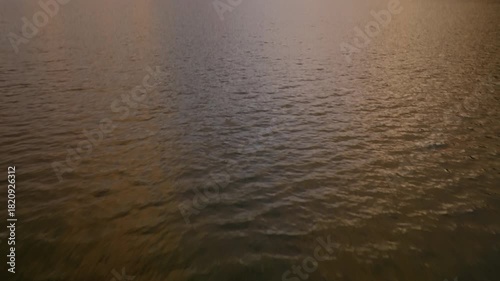 Cinematic aerial drone flight low over calm lake water tilting up to majestic mountain range at sunset. Nature landscape.