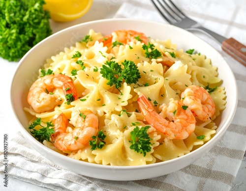 A bowl of bowtie pasta with shrimp, parsley, and lemon sits on a white cloth
