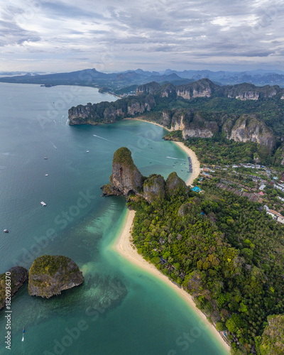 Aerial view of turquoise waters embrace jagged cliffs and lush greenery, painting a vibrant coastal scene, Railay beach, Krabi, Thailand.