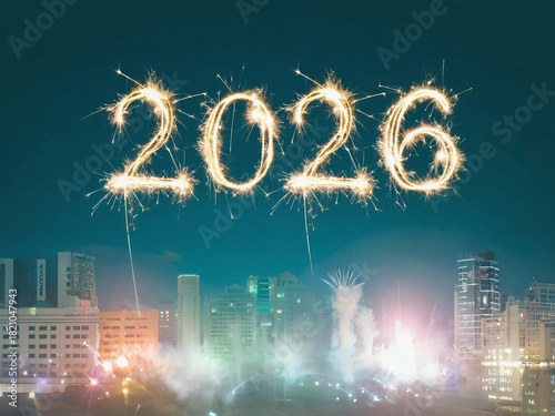 Golden sparklers for the year 2026 against a dark night sky over a blurry cityscape.