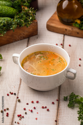 Classic chicken noodle soup with herbs served in a white bowl on rustic wooden table
