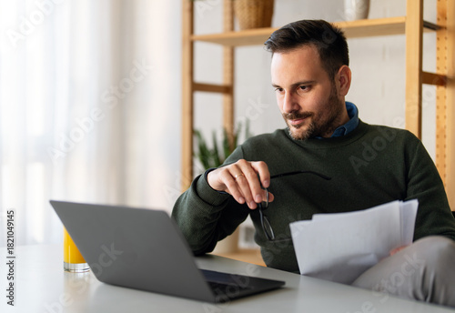 Man using smartphone and laptop computer for electronic banking, making reservation, online shopping