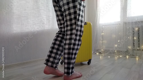 A man in sweatpants is in a room, rolling out a yellow packed suitcase