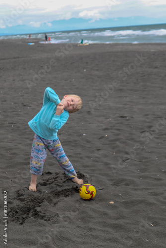 Little blond kid play football and have fun on black sand beach in Kobuleti, Georgia