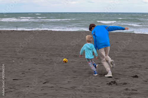 Two brothers play football and have fun on black sand beach in Kobuleti, Georgia