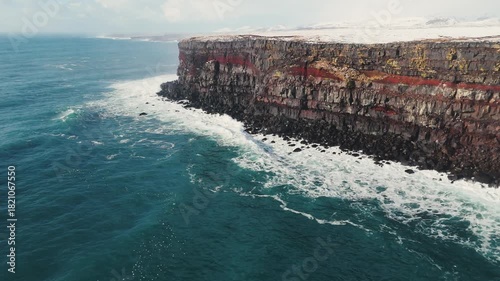 Wallpaper Mural Aerial view of storm ocean waves crashing against snowy coastal cliffs at winter sunrise. The Icelandic plateau reveals striking, martial red mineral cliffs contrasted against the icy landscape Torontodigital.ca