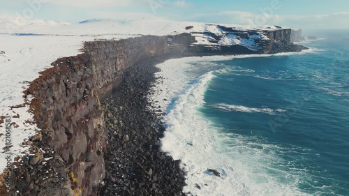 Wallpaper Mural Aerial view of storm ocean waves crashing against snowy coastal cliffs at winter sunrise. The Icelandic plateau reveals striking, martial red mineral cliffs contrasted against the icy landscape Torontodigital.ca