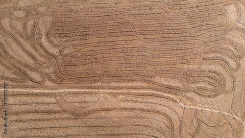Abstract aerial view of tractor tire tracks creating curved patterns on a dry soil field showing the activity of farm machinery preparation
