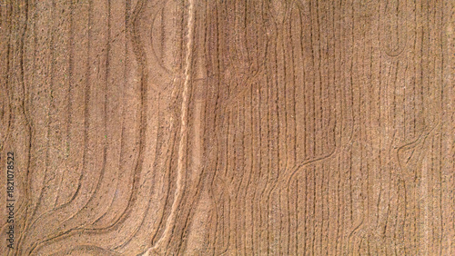 Aerial drone texture of a harvested field with straw residues and tractor tracks creating a rustic beige background pattern for agricultural themes