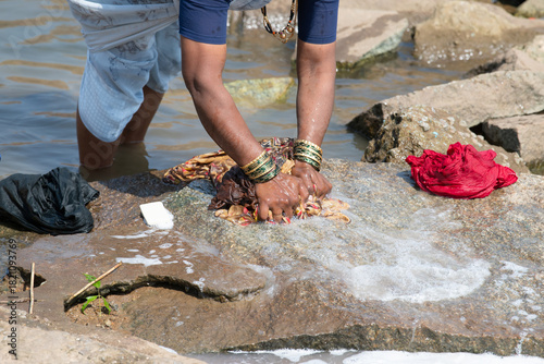 Indian woman washing clothes at Tungabhadra river, Hampi, colorful fabrics, traditional bangles on arm, lifestyle and culture of India