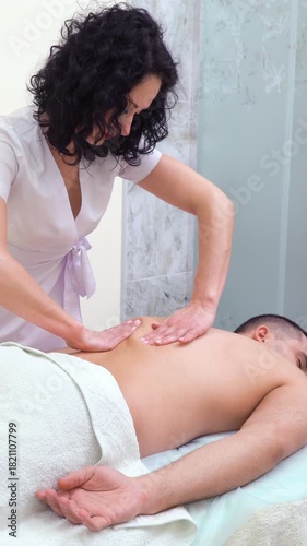 Female therapist performing relaxing back massage on client in spa, improving muscle tone, easing stress and restoring body balance