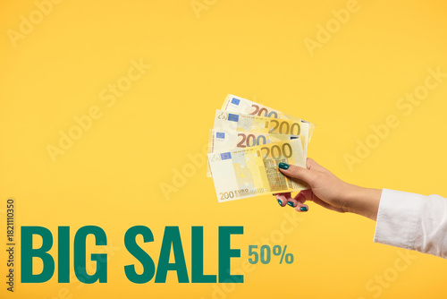 Woman hand holding euros banknotes isolated on yellow background. Finance concept.