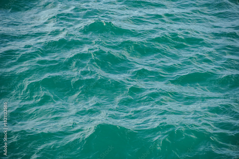 Obraz premium Sea wave texture close up. Dark blue water surface with ripples background. macro blue wave pattern in a river with motion blur. Sparkling sunlight reflecting on the surface of a calm.