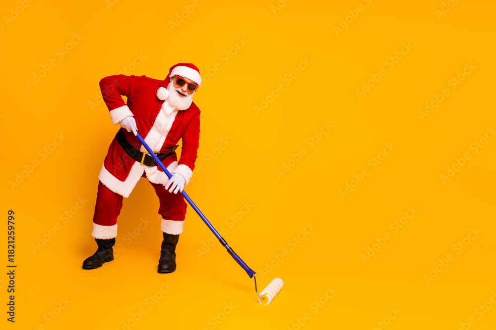 Obraz premium Santa in red suit paints holiday vibes with roller yellow background capturing merry season spirit and playful home style for festive stock photo