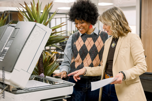 Diverse businesswomen using office photocopier collaborating at work
