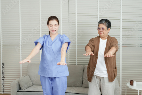 Asian female physical therapist demonstrates forward arm stretch while senior asian woman follows instructions during upper body rehabilitation training in clinic setting