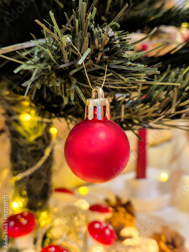 A red bauble on the Christmas tree. Festive decorations and a glowing garland with warm light.