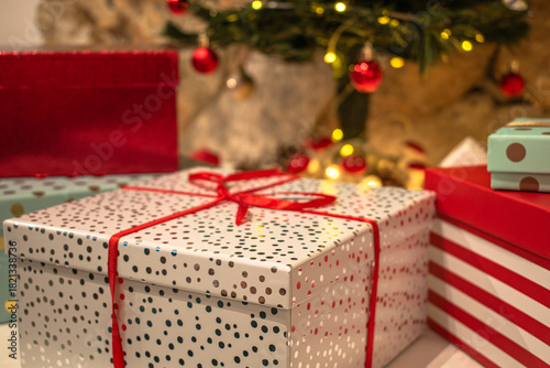 Christmas gifts, bright boxes with ribbons. A candle and festive decorations in the background.