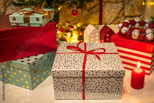 Christmas gifts, bright boxes with ribbons. A candle and festive decorations in the background.