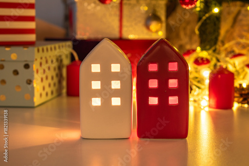 Ceramic miniature houses with candles inside. Gifts wrapped in paper. Christmas decorations and a garland glowing with warm light.