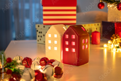 Ceramic miniature houses with candles inside. Gifts wrapped in paper. Christmas decorations. A jingle bell wreath and a garland glowing with warm light.