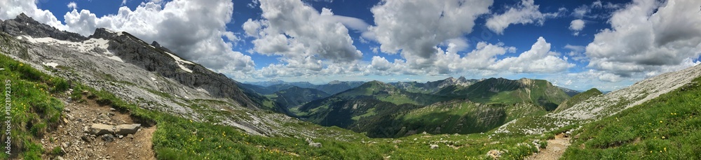 Obraz premium Panoramic rocky mountain trail with vibrant meadows under a clear blue sky