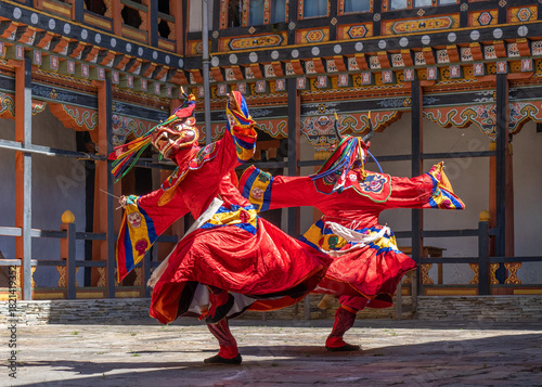 Jakar, Bhutan - 24 September 2025: View of vibrant red-clad dancers performing with graceful movements against the backdrop of intricately carved, colorful architecture in Bumthang.