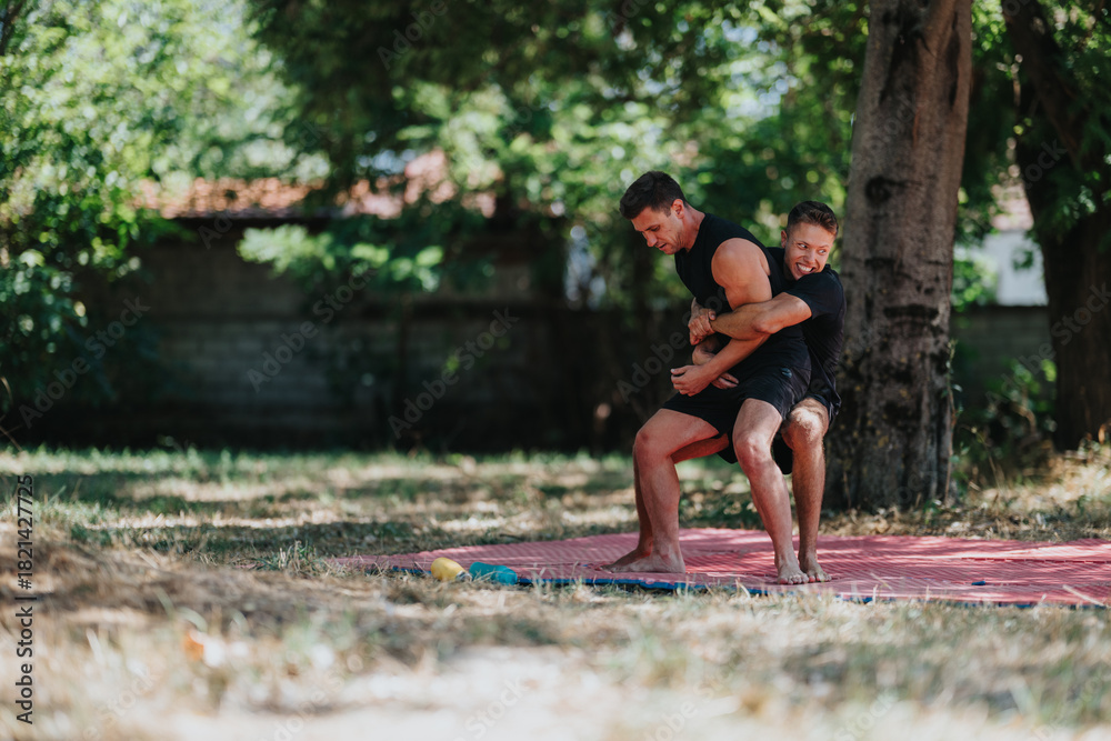 Obraz premium Two men wrestle on a red mat in a sunlit park, displaying strength, teamwork, and competitive fitness. Ideal for sports, outdoor activity, and athletic training themes.