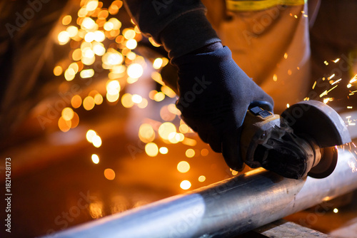 Close-up of a worker using an angle grinder on metal, producing bright sparks. The image illustrates industrial manufacturing and metalworking processes.