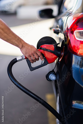 Close-up of a person’s hand holding a fuel pump nozzle while refueling a car at a gas station. The image shows transportation, energy, and daily vehicle usage.