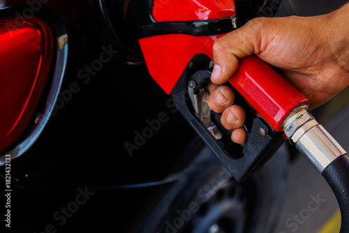 Close-up of a person’s hand holding a fuel pump nozzle while refueling a car at a gas station. The image shows transportation, energy, and daily vehicle usage.