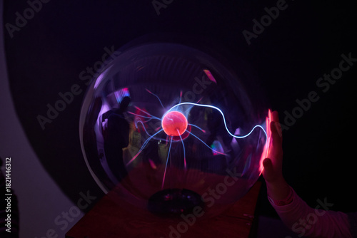 A person touching a plasma ball in a dark room.