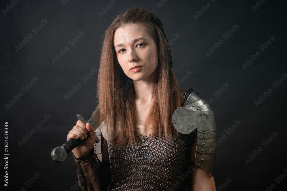 Naklejka premium Portrait of a young woman, fantasy warrior in armor with a sword in her hands isolated on a dark background.