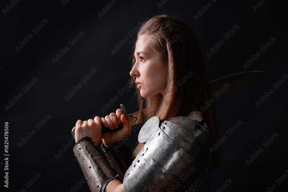 Fototapeta premium Portrait of a young woman, fantasy warrior in armor with a sword in her hands isolated on a dark background.